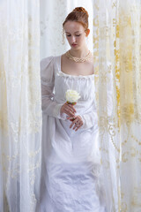 A Regency period woman wearing a white embroidered cotton dress and surrounded by backlit lace...