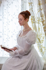 A Regency period woman wearing a white embroidered cotton dress and surrounded by backlit lace...