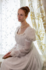A Regency period woman wearing a white embroidered cotton dress and surrounded by backlit lace...
