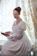 A Regency period woman wearing a white embroidered cotton dress and surrounded by backlit lace...