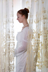 A Regency period woman wearing a white embroidered cotton dress and surrounded by backlit lace...