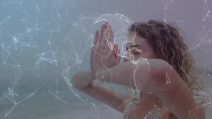 Yogi by sea raising palms activating spinning globe overlay highlighting global health connections - Powered by Adobe