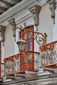Ornate balcony with decorative wrought iron railing and terracotta flower pots, showcasing architectural beauty in Cuenca, Ecuador, under a clear blue sky