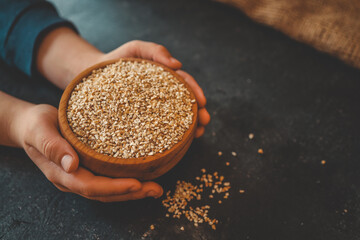 Hands holding a wooden bowl filled with raw steel-cut oats on a dark surface. Healthy food concept...
