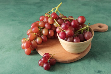 Bowl and wooden board with tasty ripe grapes on green background