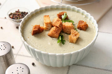 Bowl of tasty cream soup with croutons on white tile background