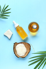 Bottles of coconut cosmetic oil with plant leaves on blue background