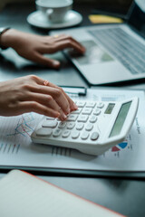 Close-up of hands using a calculator and laptop, analyzing financial data in a modern office...