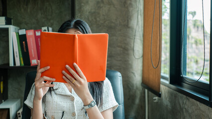 A woman sits in a modern office, reading a book by the window, surrounded by stylish decor and natural light.