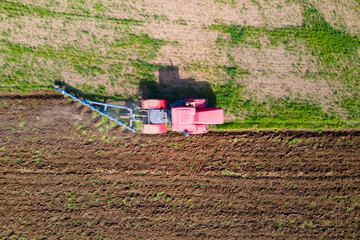 Aerial shot of a red tractor plowing a green and brown field, creating a striking contrast of colors. perfect representation of modern agriculture and rural landscapes.