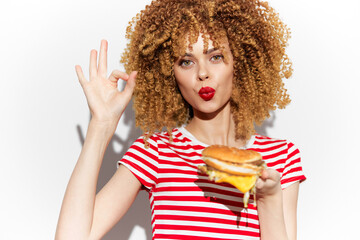 Happy woman with curly hair enjoying a delicious burger, wearing a striped shirt, expressing joy and satisfaction, perfect for food and lifestyle themes