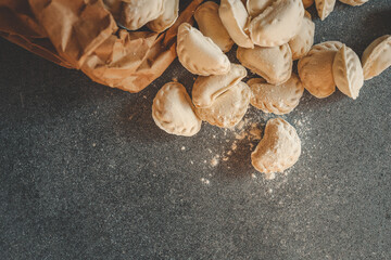 Frozen tortellini pasta spilling out of a brown paper bag onto a dark stone surface, ready for cooking or packaging