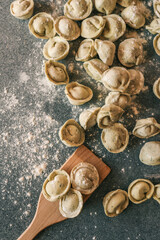 Top view of raw dumplings scattered on a floured countertop with a wooden spatula, capturing a rustic and homely food preparation scene