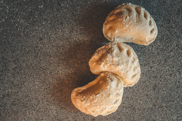 Three raw homemade dumplings sprinkled with flour on dark countertop, traditional Eastern European food before boiling