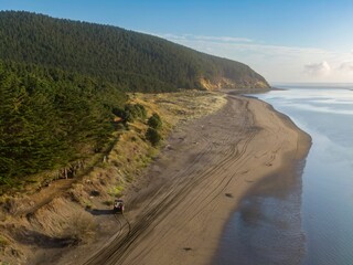 A couple drives an ATV along a sandy beach in Aotea, Kawhia, Waikato, New Zealand. They are enjoying a recreational activity, exploring the coastline and enjoying the scenery.