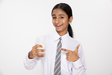 Indian school girl pointing finger to milk glass in hand on studio