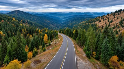 Scenic mountain road winding through colorful forested hills under a cloudy sky