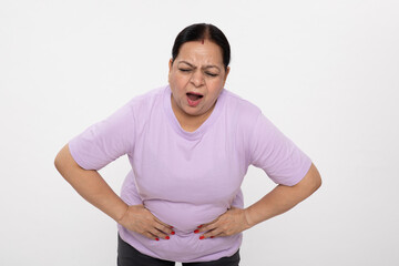 Portrait of an indian unhealthy senior woman holding her stomach pain, abdominal pain, eating...