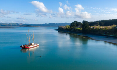 A traditional waka, a double-hulled canoe, rests on calm waters near the shore in New Zealand. The...