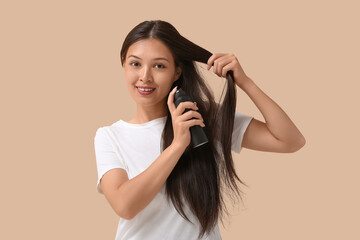 Beautiful young happy woman applying hair spray on beige background