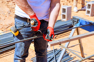 Construction worker grips metal rebar cuts while wearing gloves on busy building site.