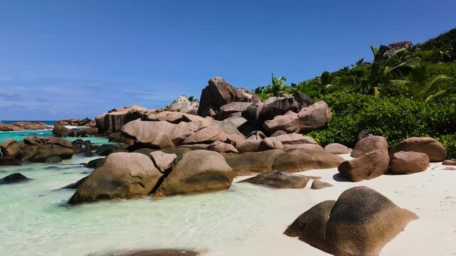 Granite boulders rise from a white sandy beach surrounded by lush tropical greenery and turquoise waters. Anse Cocos. Seychelles, La Digue.