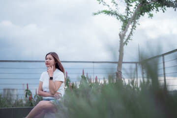 Young woman sits contemplatively in a rooftop garden, her hand gently touching her face as she...