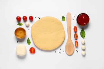 Rolled out dough, wooden spoon and ingredients for preparing pizza with mozzarella on white background
