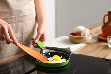 Woman frying quail eggs on electric stove in kitchen, closeup