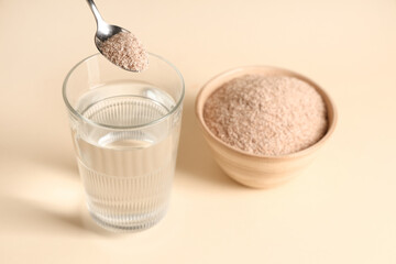 Glass of water and spoon with psyllium husk on beige background