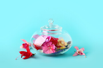 Glass jar with different beautiful edible flowers on blue background