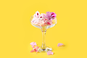Glass with different beautiful edible flowers on yellow background