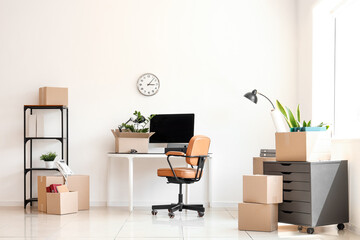 Interior of office with workplace, shelf unit and cardboard boxes on moving day
