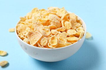 Bowl with tasty cornflakes on blue background, closeup
