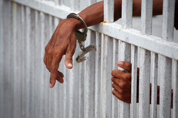Hands of Inmate in Handcuffs Reaching Through Jail Bars