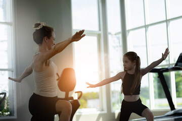 Cheerful mother little daughter standing in living room at home moving yoga together. Child have fun with elder sister nanny or loving mother active leisure and lifestyle concept