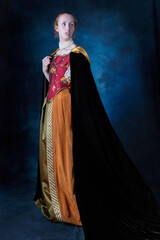 A red-haired Renaissance woman wearing an embroidered silk ensemble against a studio backdrop