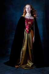 A red-haired Renaissance woman wearing an embroidered silk ensemble against a studio backdrop