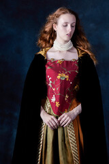 A red-haired Renaissance woman wearing an embroidered silk ensemble against a studio backdrop