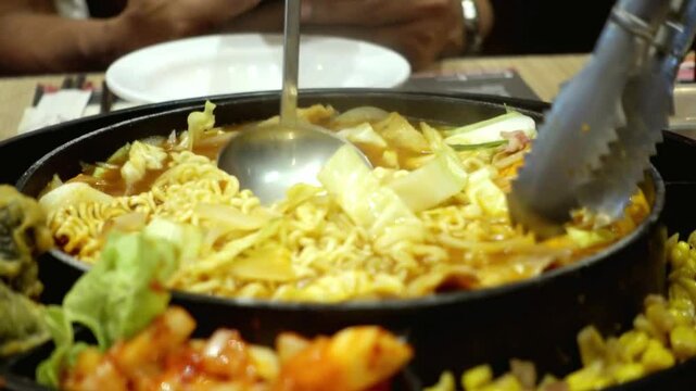 Close-up shot of people cooking and eating Korean Budae Jjigae