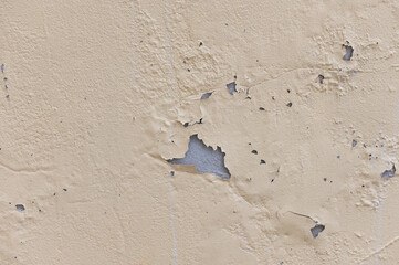 Close-up of a weathered beige wall showing peeling paint, surface cracks, and exposed underlayer, highlighting decay and texture.
