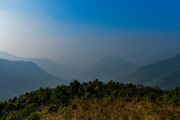 Hazy mountains covered in dense forests under a clear blue sky in Meghalaya. 