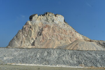 Large rock formation with varied textures and colors against a blue sky in Meghalaya. 