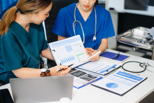 Two doctors and a female nurse meet at a table in the hospital, collaborating on medical tasks using laptops and computers