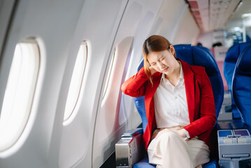 Photo of a frustrated woman sitting on an airplane with her head in her hands. Asian woman sitting...