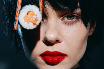 Stylish model with sushi and bold makeup, showcasing a unique culinary concept and urban flair in a dramatic lighting setup.