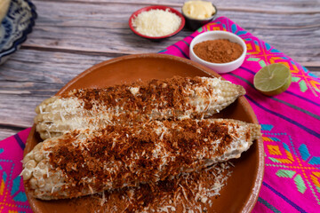 Two corn cobs topped with chili, cheese, and mayonnaise, served on a table as a traditional Mexican dish.