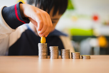 An Asian boy arranges a stack of coins, topped by a human model, symbolizing the crucial concept of learning investment from childhood.