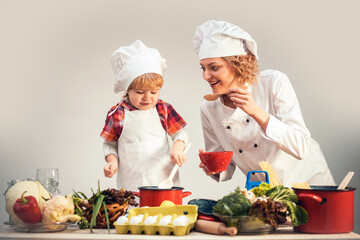 Mother and child chef cook cooking together. Kid chef cook helping mother to cooking. Mother and son cooking healthy food. Mother chef cook with apron and baby chef cook isolated in studio.