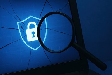 Close-up of Cracked Laptop Screen with Magnifying Glass Highlighting Locked Security Shield Icon in Blue Background